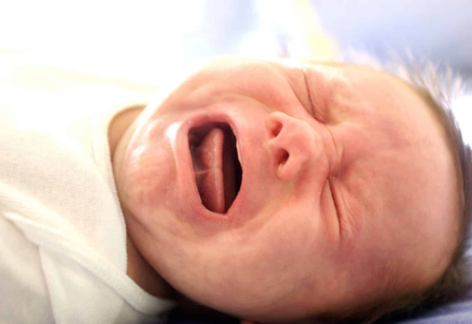 A swaddled newborn crying with mouth wide open, showing the tongue and palate.