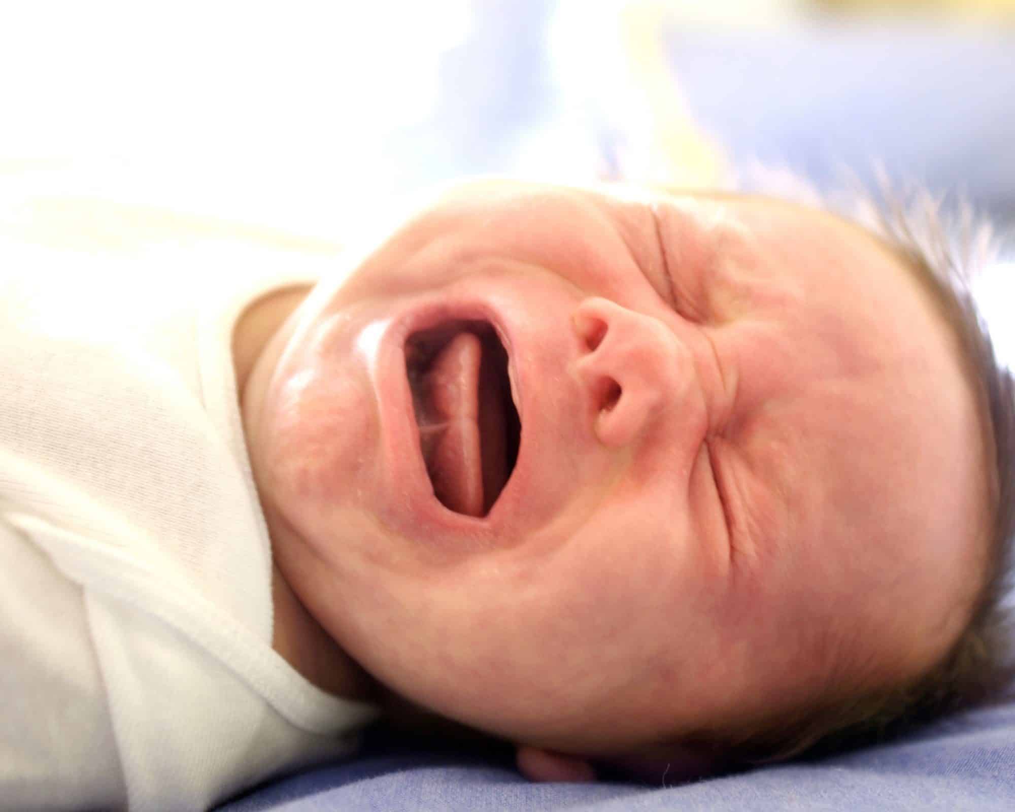 A swaddled newborn crying with mouth wide open, showing the tongue and palate.