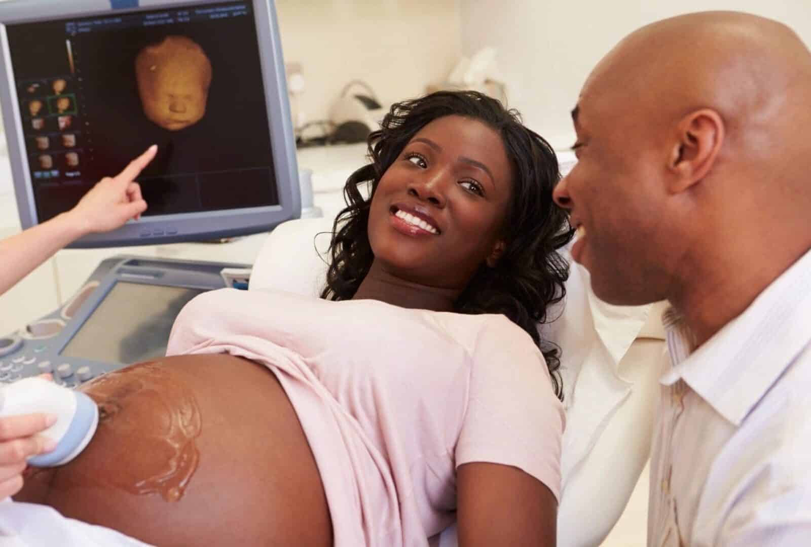 A pregnant woman and her partner smiling at an ultrasound screen during a prenatal appointment.