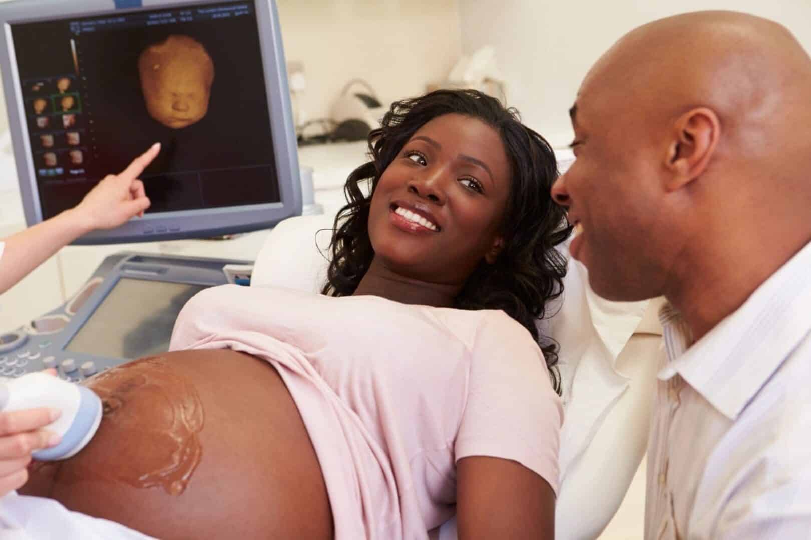 A pregnant woman and her partner smiling at an ultrasound screen during a prenatal appointment.