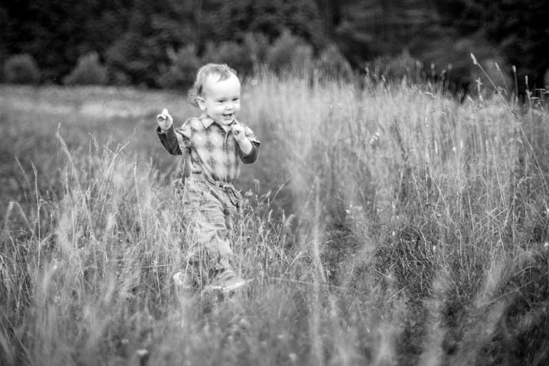 A smiling toddler taking early steps through a grassy field.