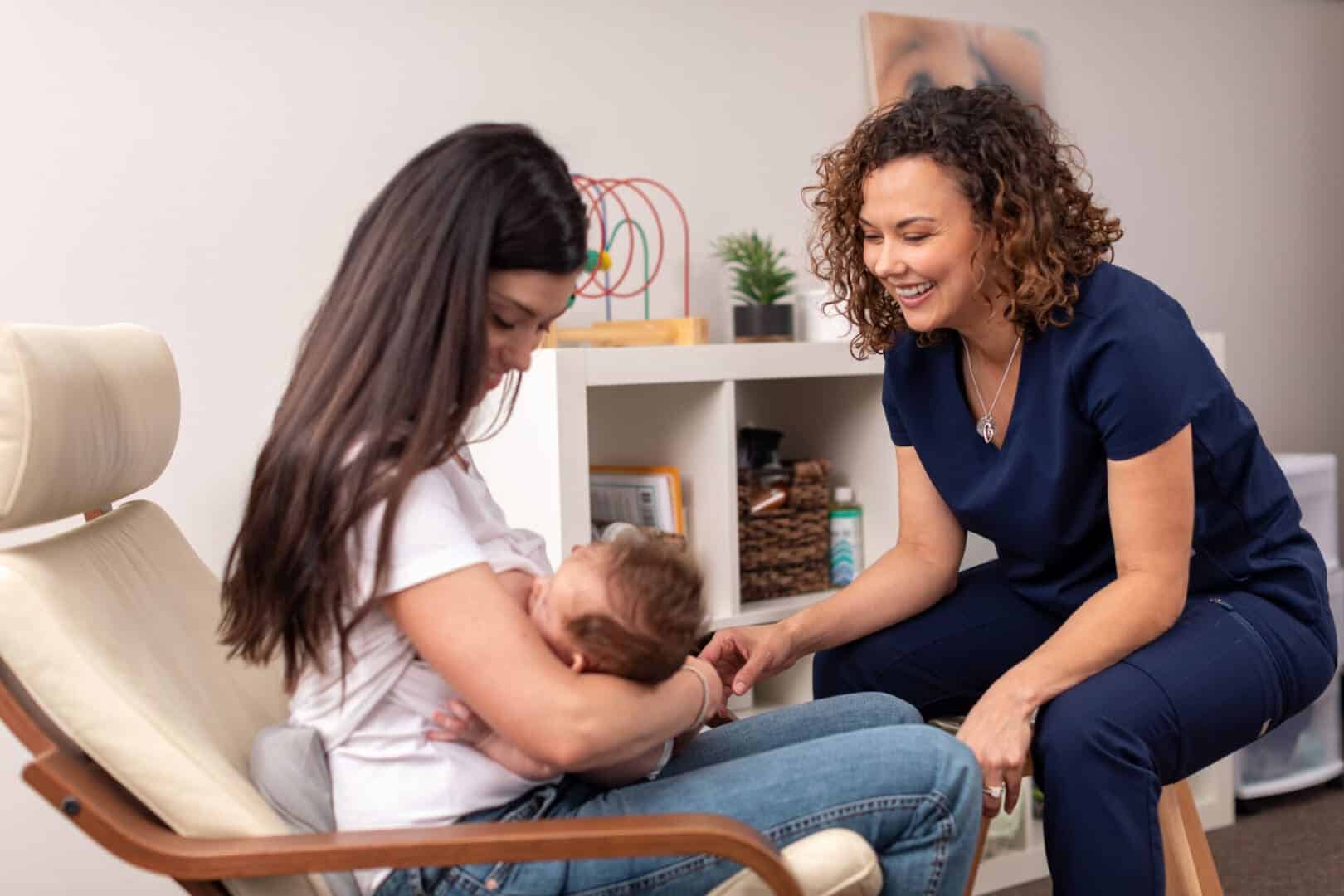 An IBCLC sitting with a mother as she nurses her newborn during an office lactation visit.