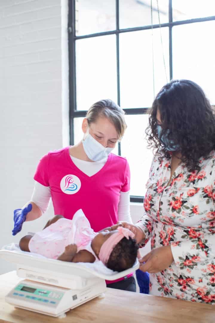 An IBCLC weighing a baby on an infant scale while the mother looks on.