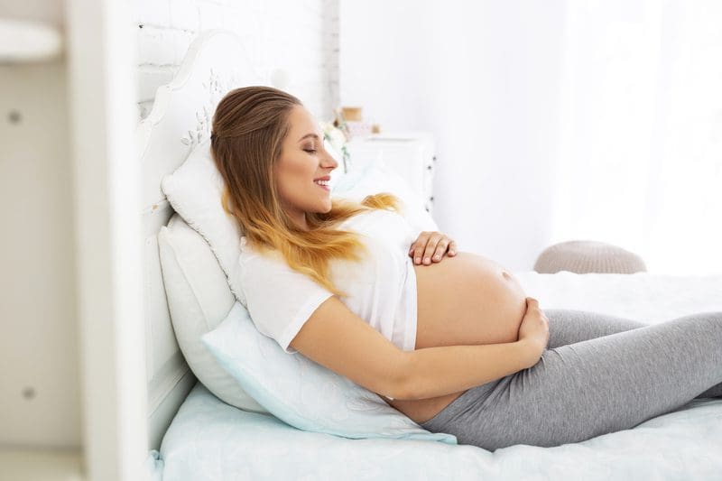 a pregnant woman lying on the bed and smiling