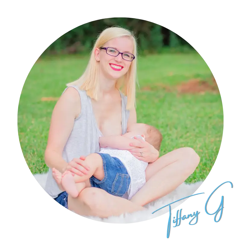 A woman with glasses holding a baby in the grass.