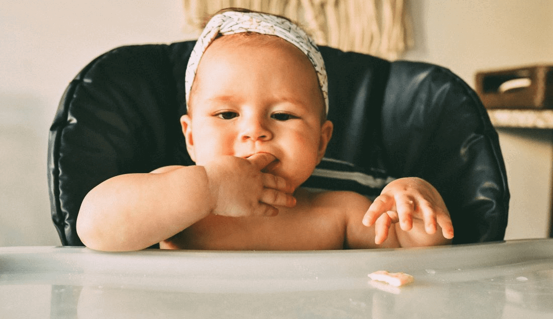 A baby sitting in a high chair ready to try solid foods.