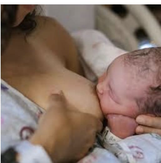 Mother breastfeeding newborn baby in hospital bed.