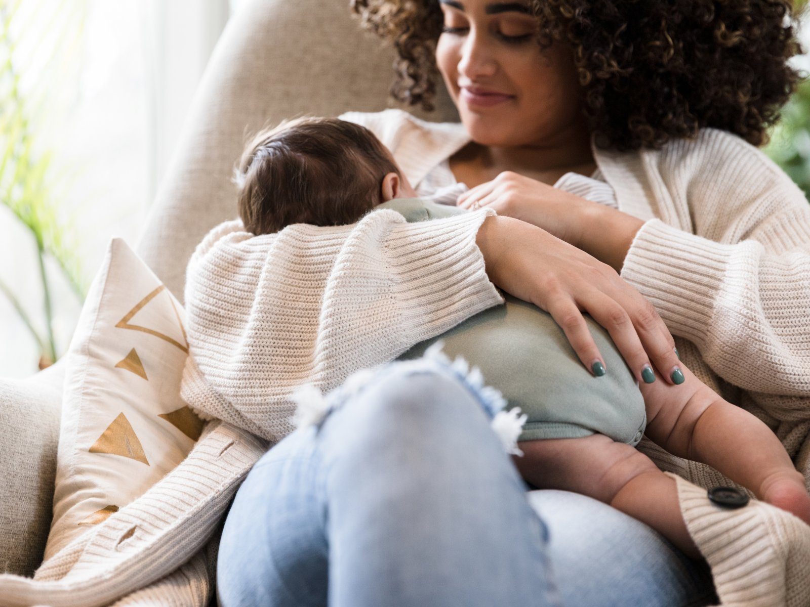 A parent holding their sleeping baby close in a cozy armchair during a feeding