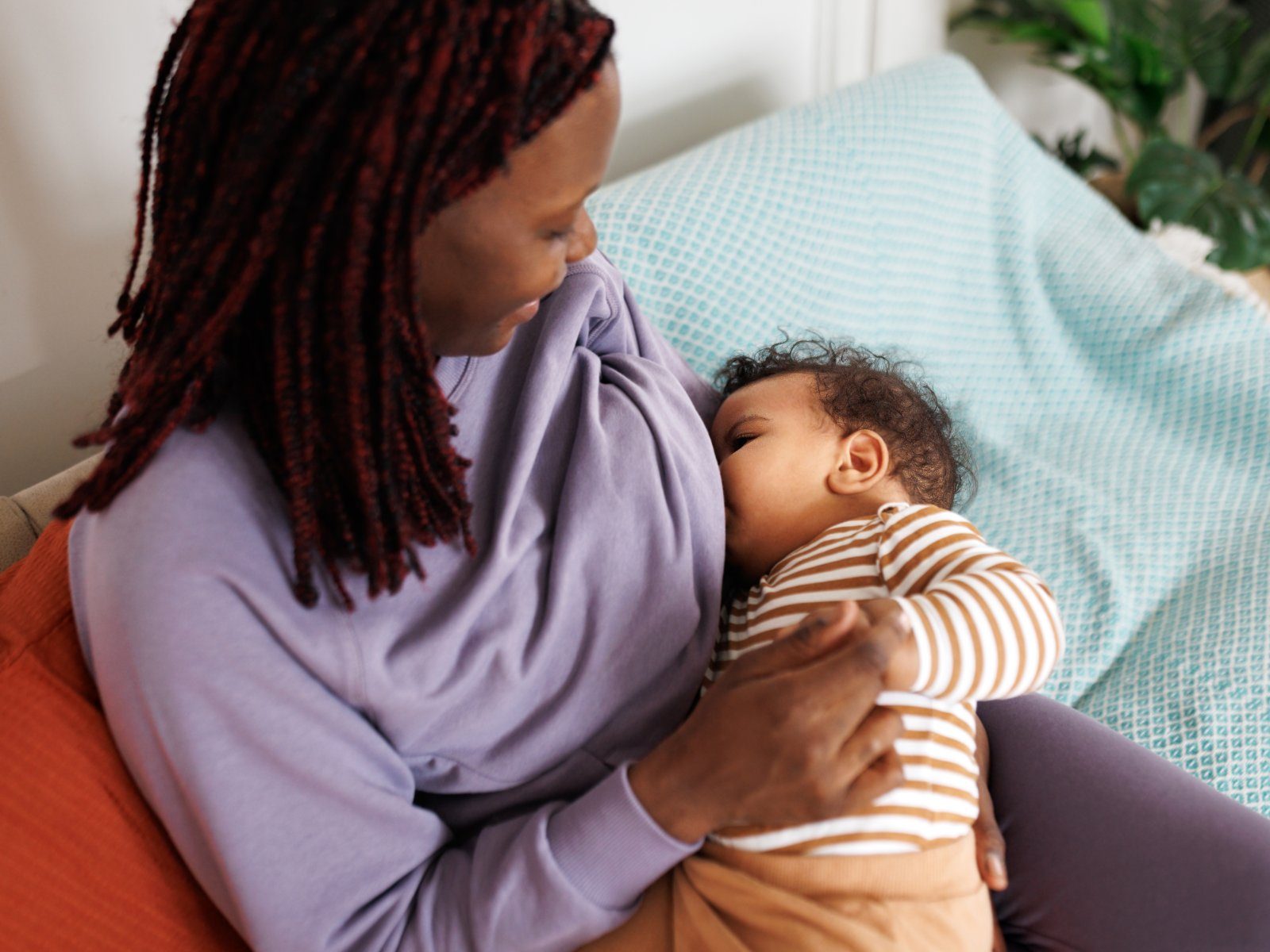 A parent breastfeeding their baby while sitting on a sofa at home