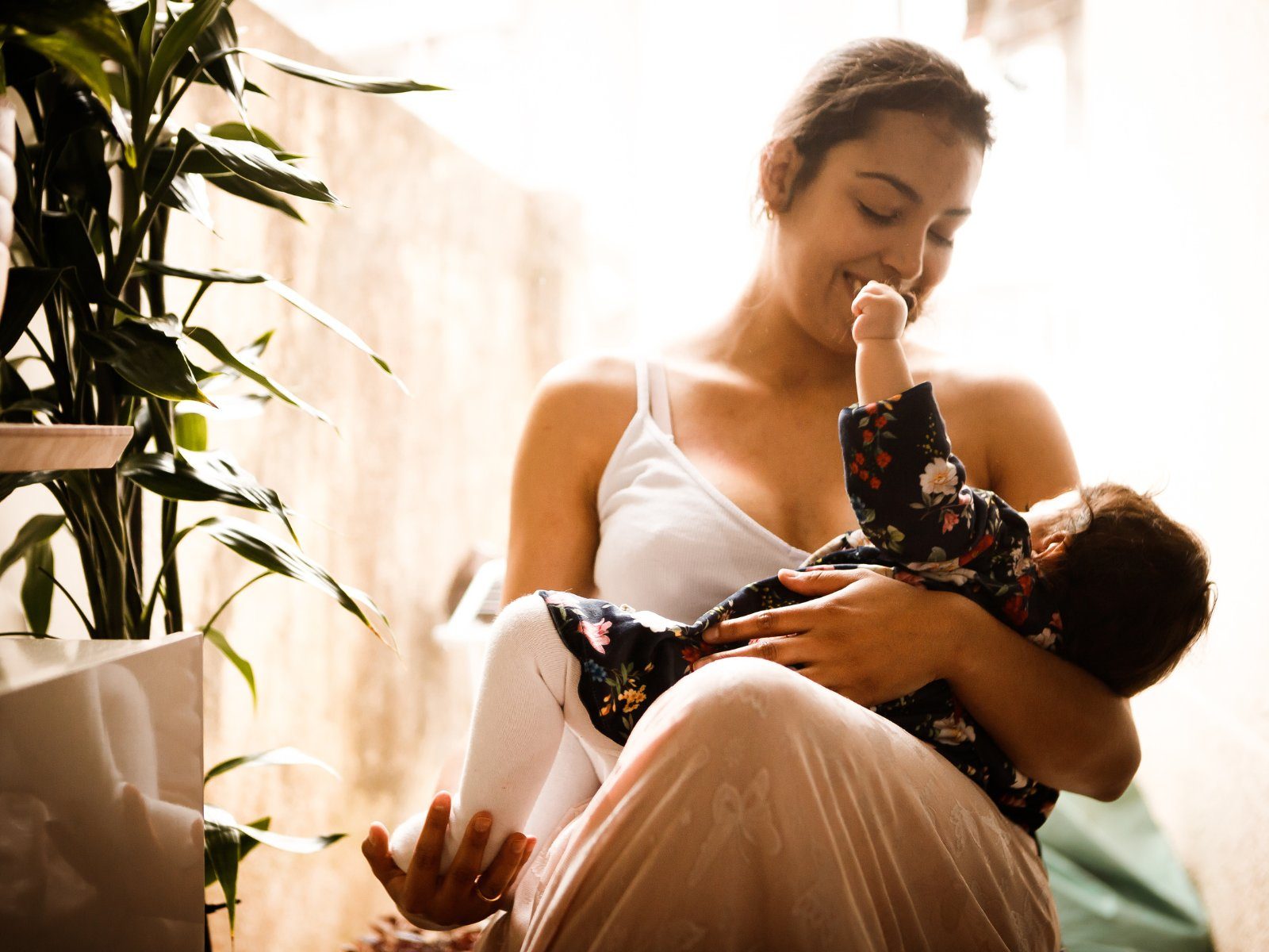A smiling parent cradling their baby in a sunlit room during a feeding