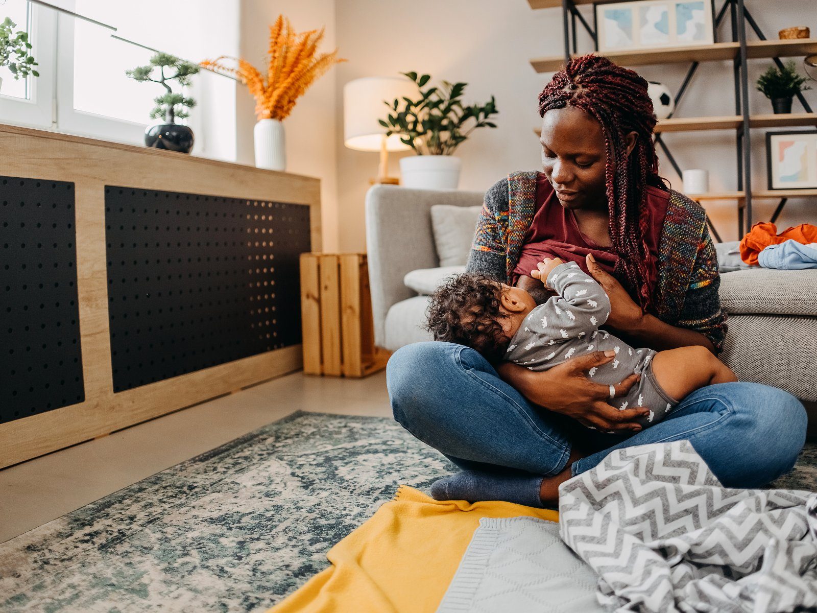 A parent nursing their baby while sitting on the living-room floor at home