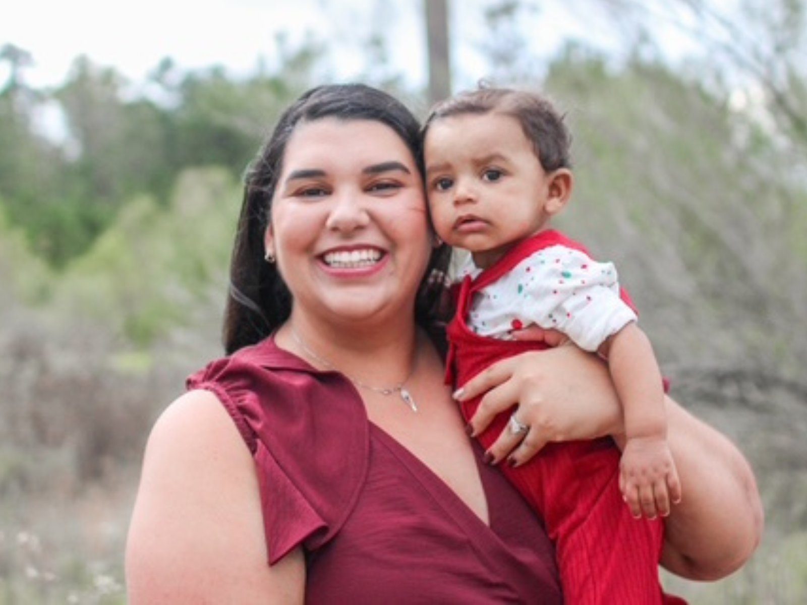 A smiling parent holding their baby outdoors