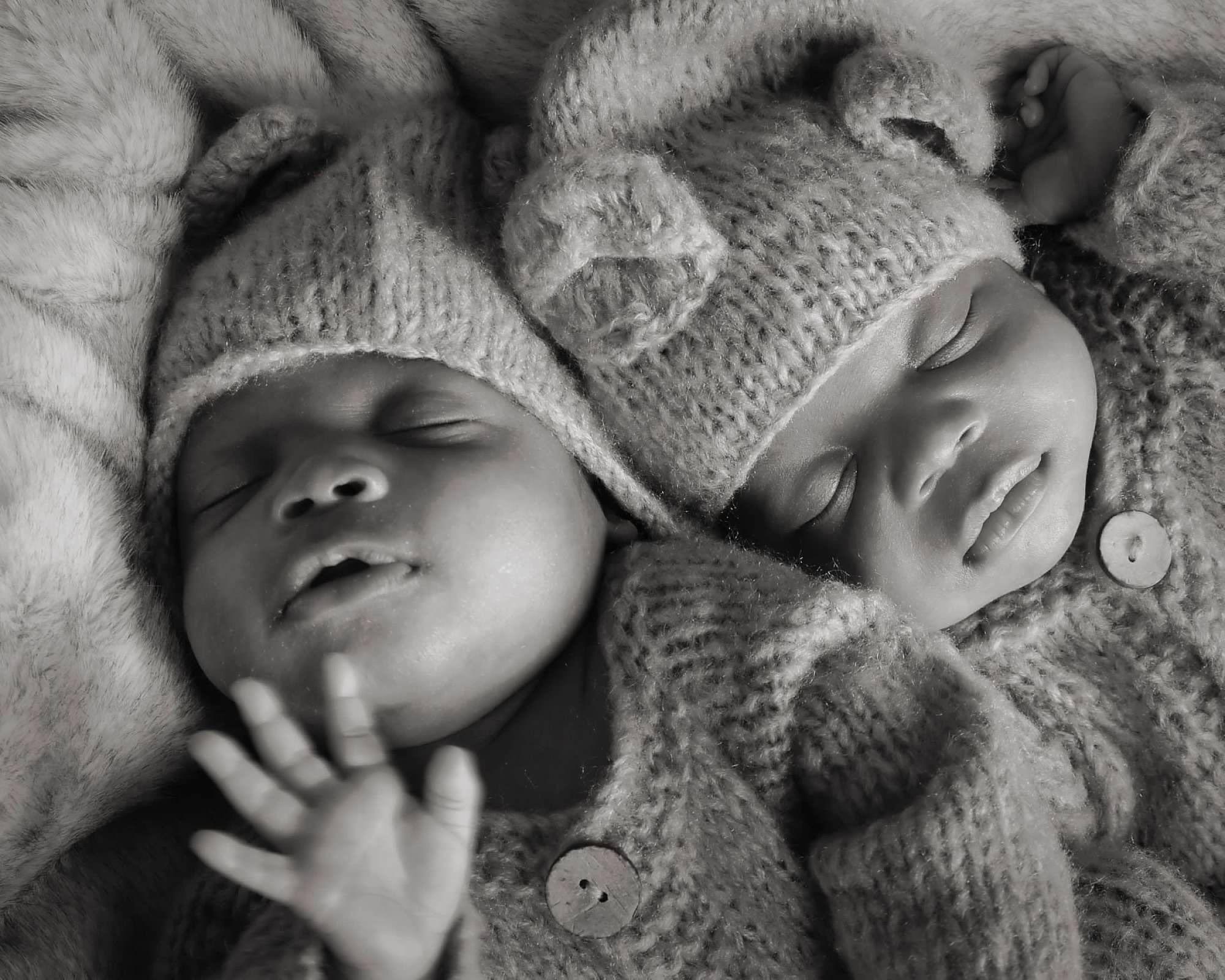 Two newborns sleeping peacefully, swaddled in knit