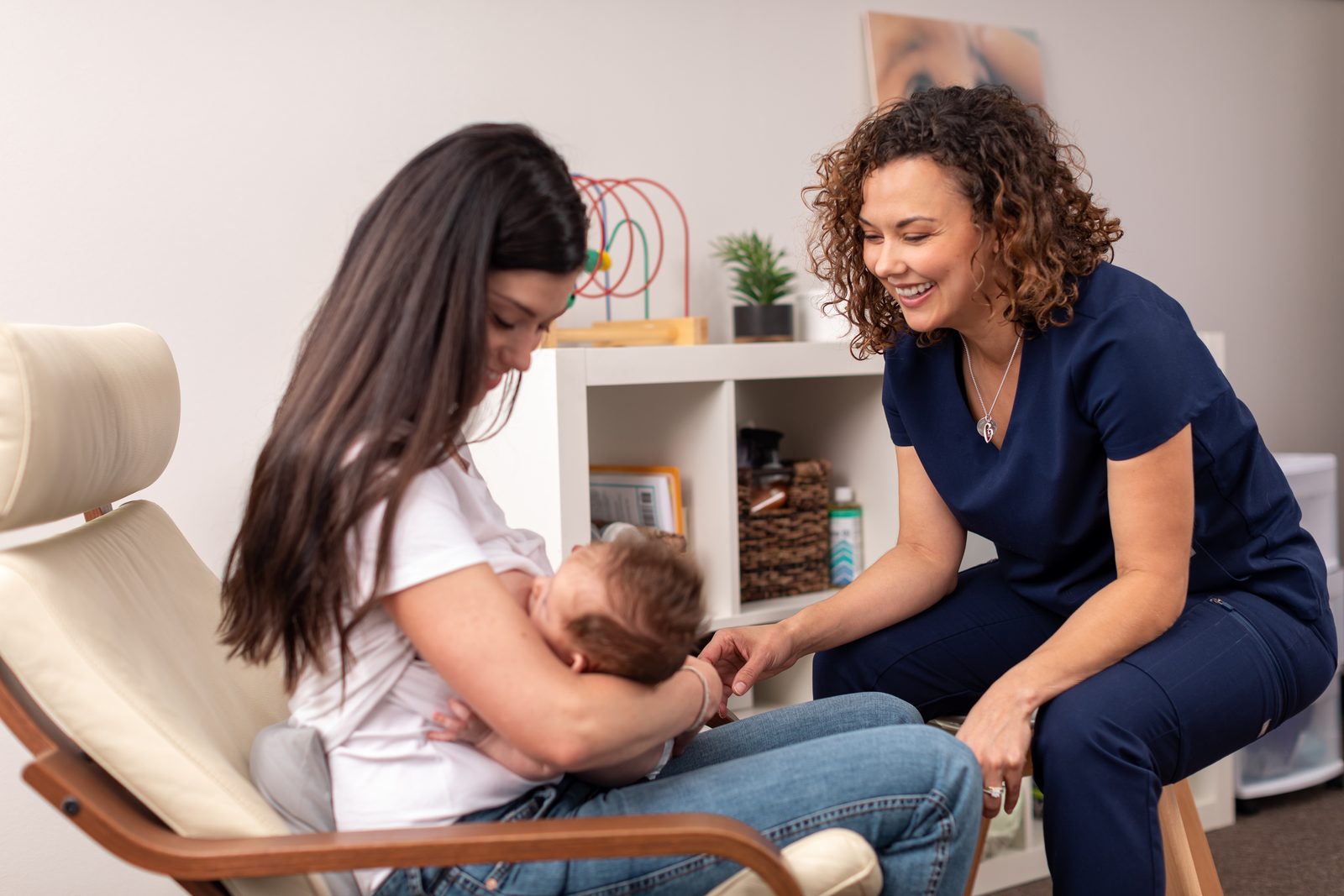An IBCLC sitting with a parent and baby, supporting a comfortable feed during a lactation consultation.