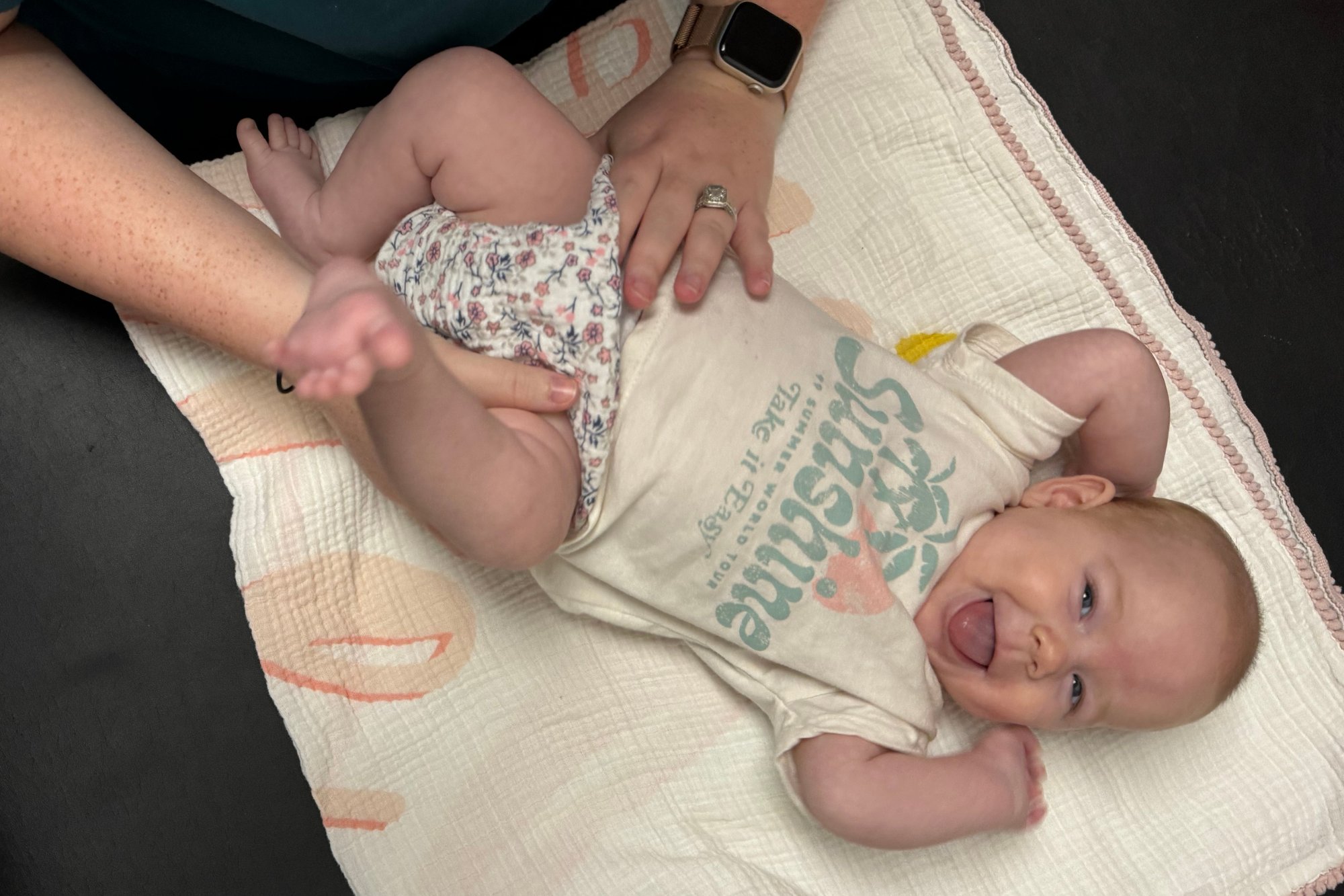 A smiling infant lying down while a practitioner provides a gentle chiropractic adjustment
