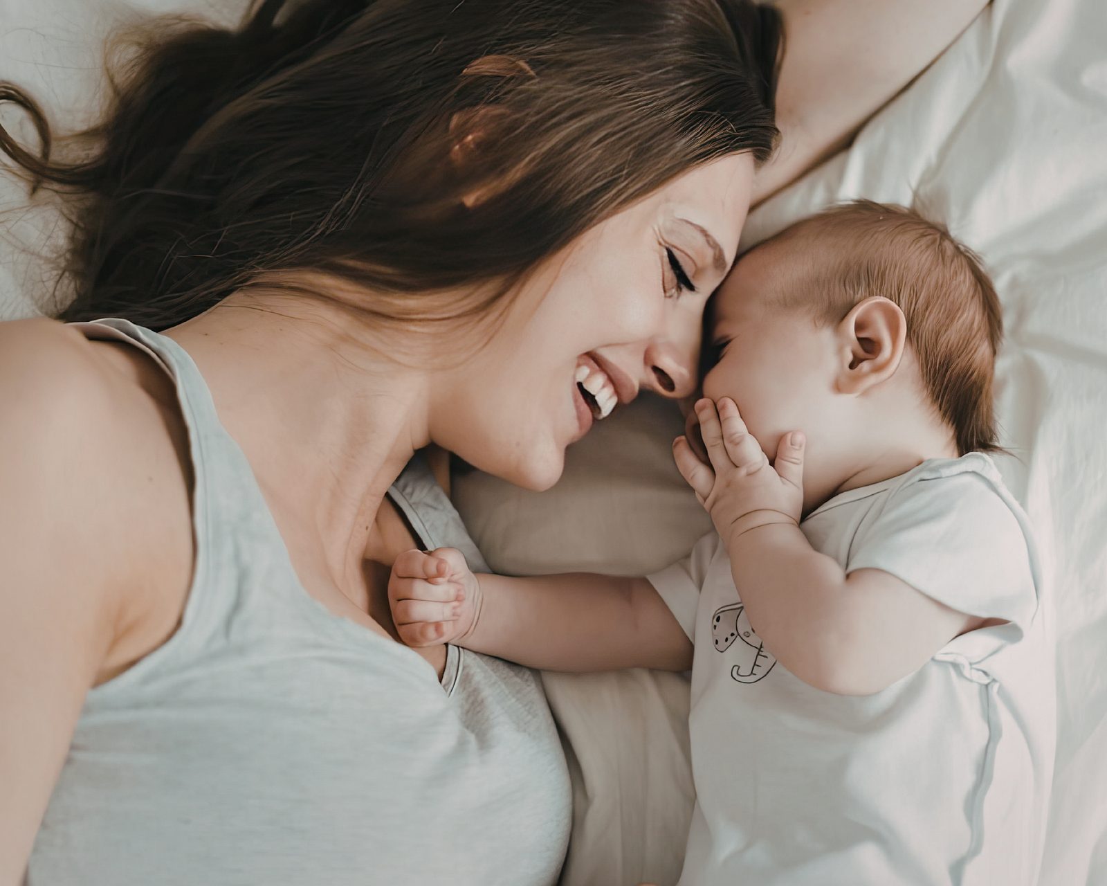 A smiling parent lying nose-to-nose with a baby, both relaxed and content