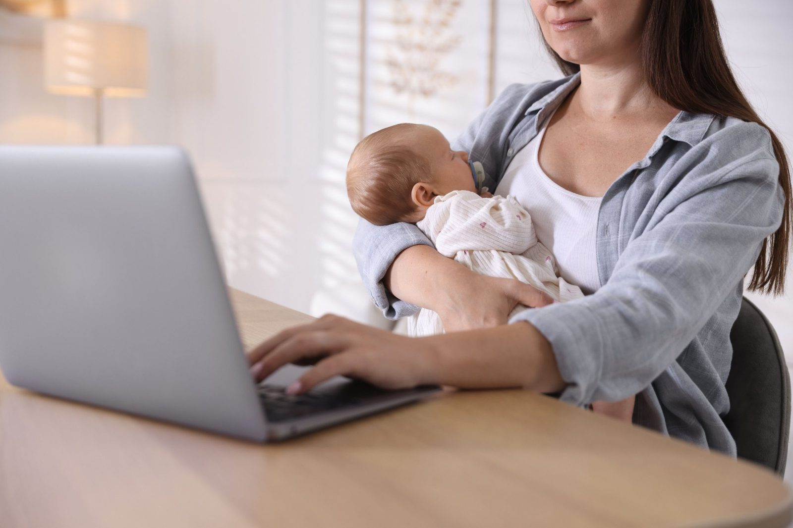 A mother holding her sleeping baby during a virtual lactation visit on her laptop at home