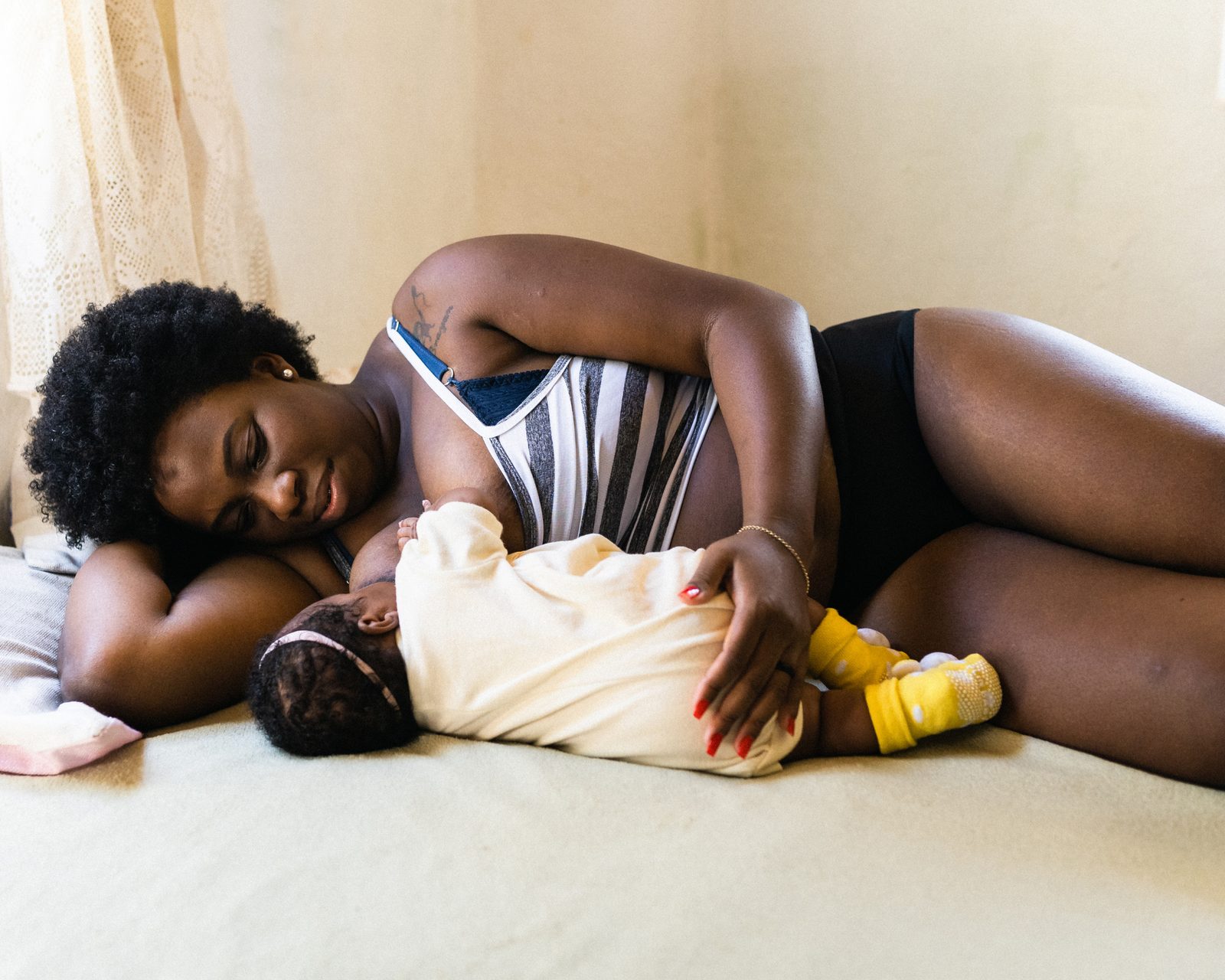 A parent breastfeeding their baby while resting together on a bed