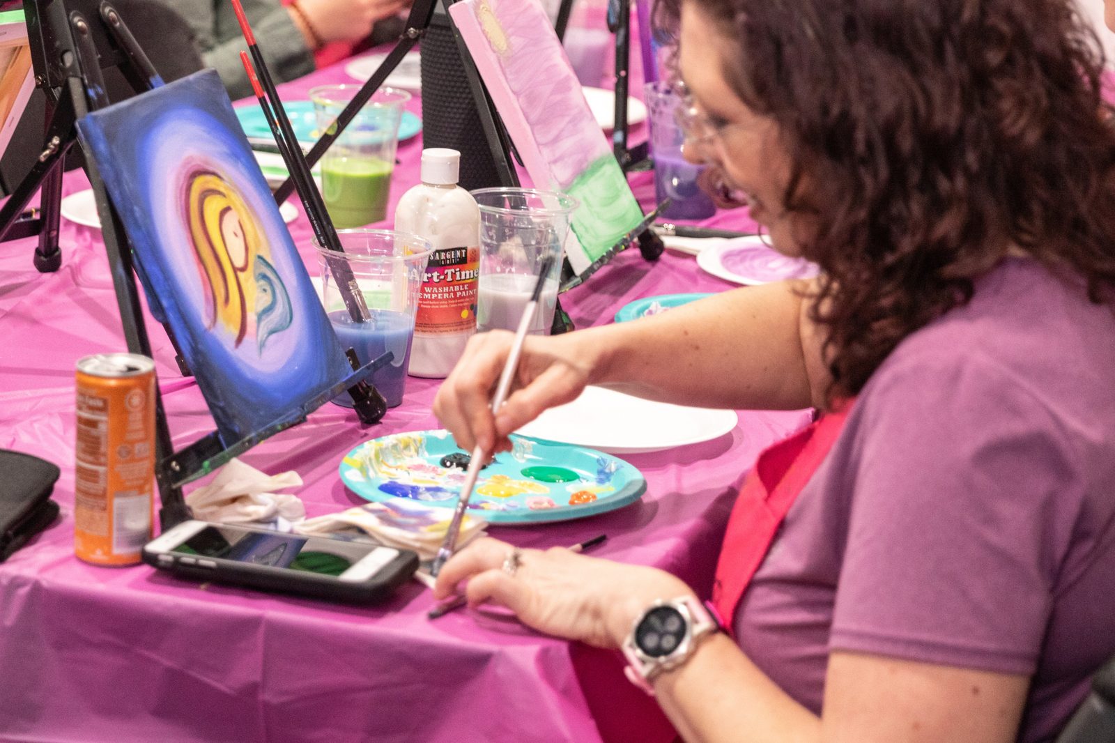Suzanne Juel painting a mother-and-baby canvas, holding a brush and palette at her easel