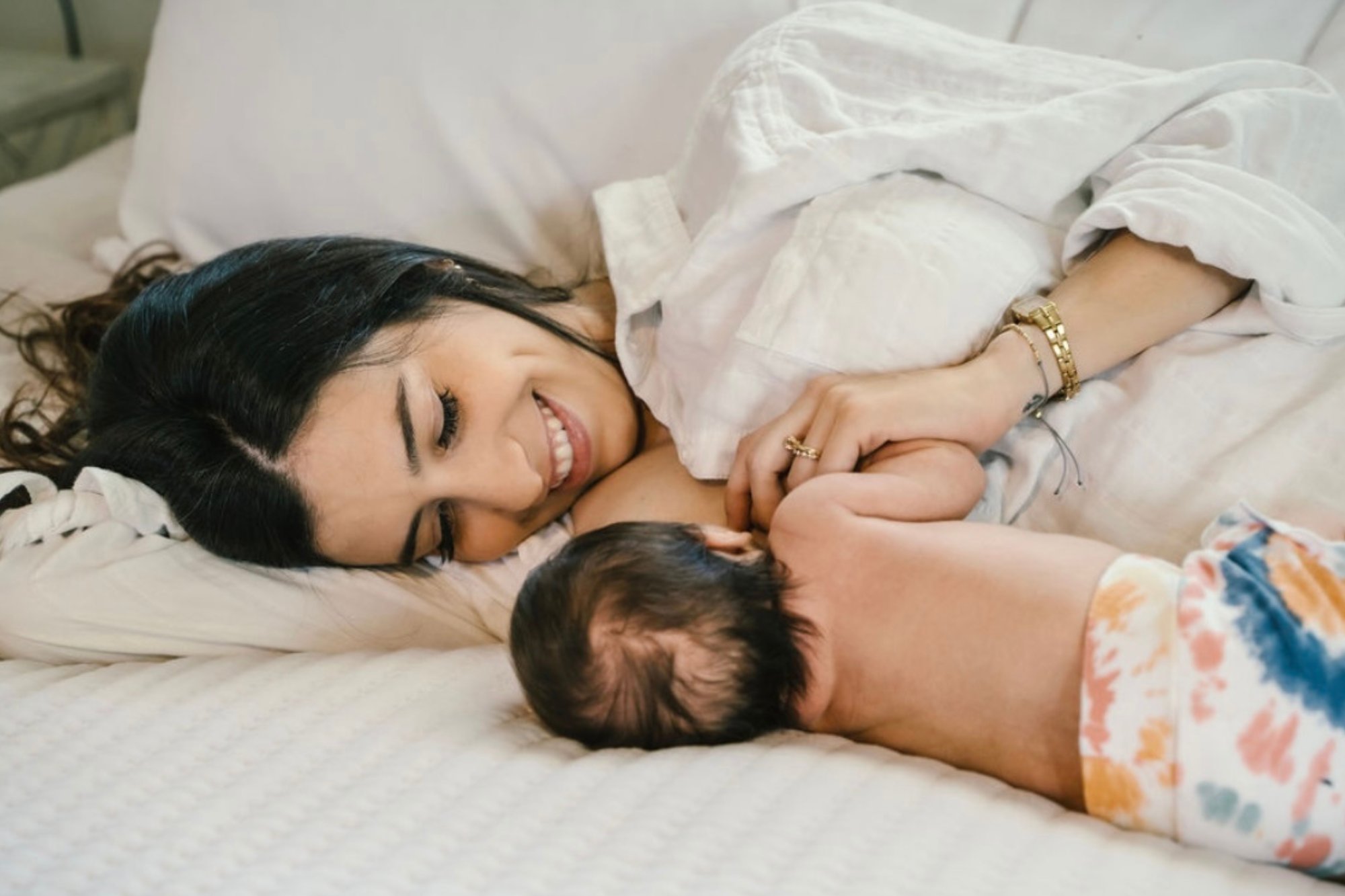 A parent breastfeeding their newborn at the bedside during an early postpartum lactation visit