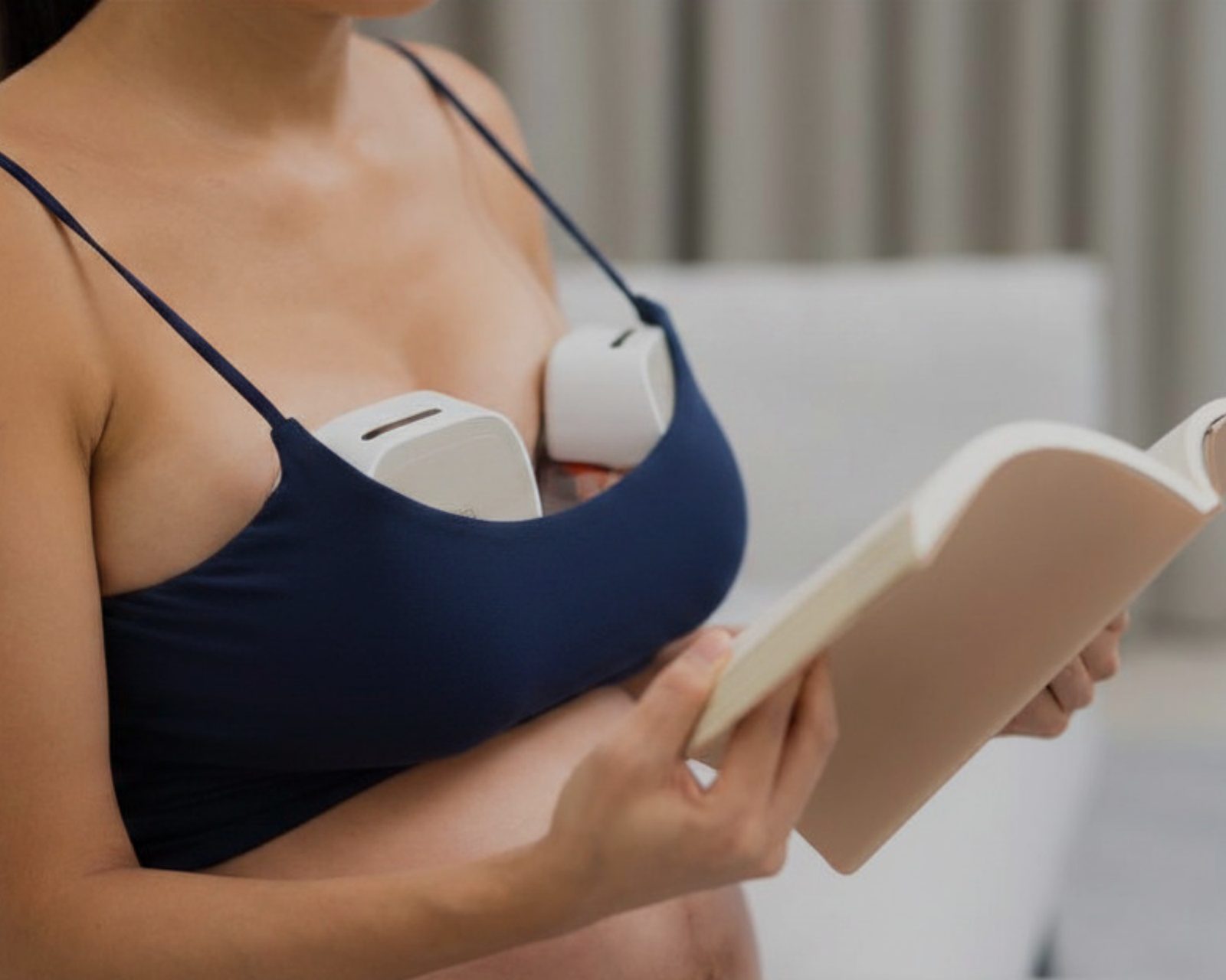 A parent using a hands-free wearable breast pump while reading at home