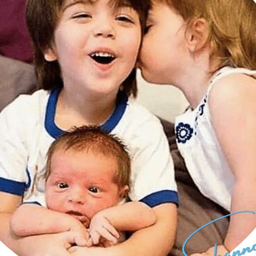 A child kissing a sibling while holding a newborn.