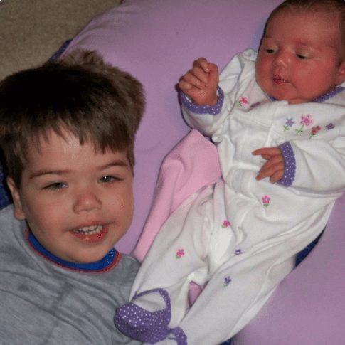 A toddler sitting beside a swaddled newborn.