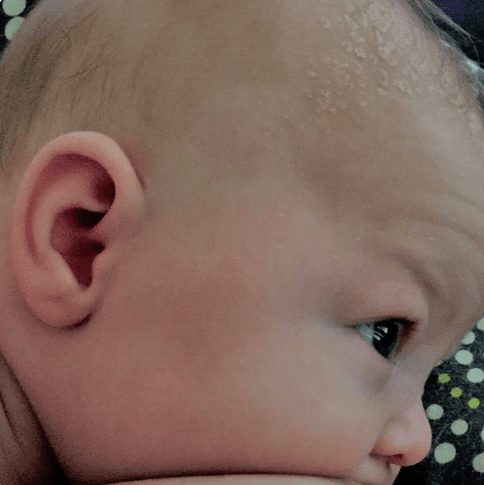 A baby latched and nursing against a mother's chest.