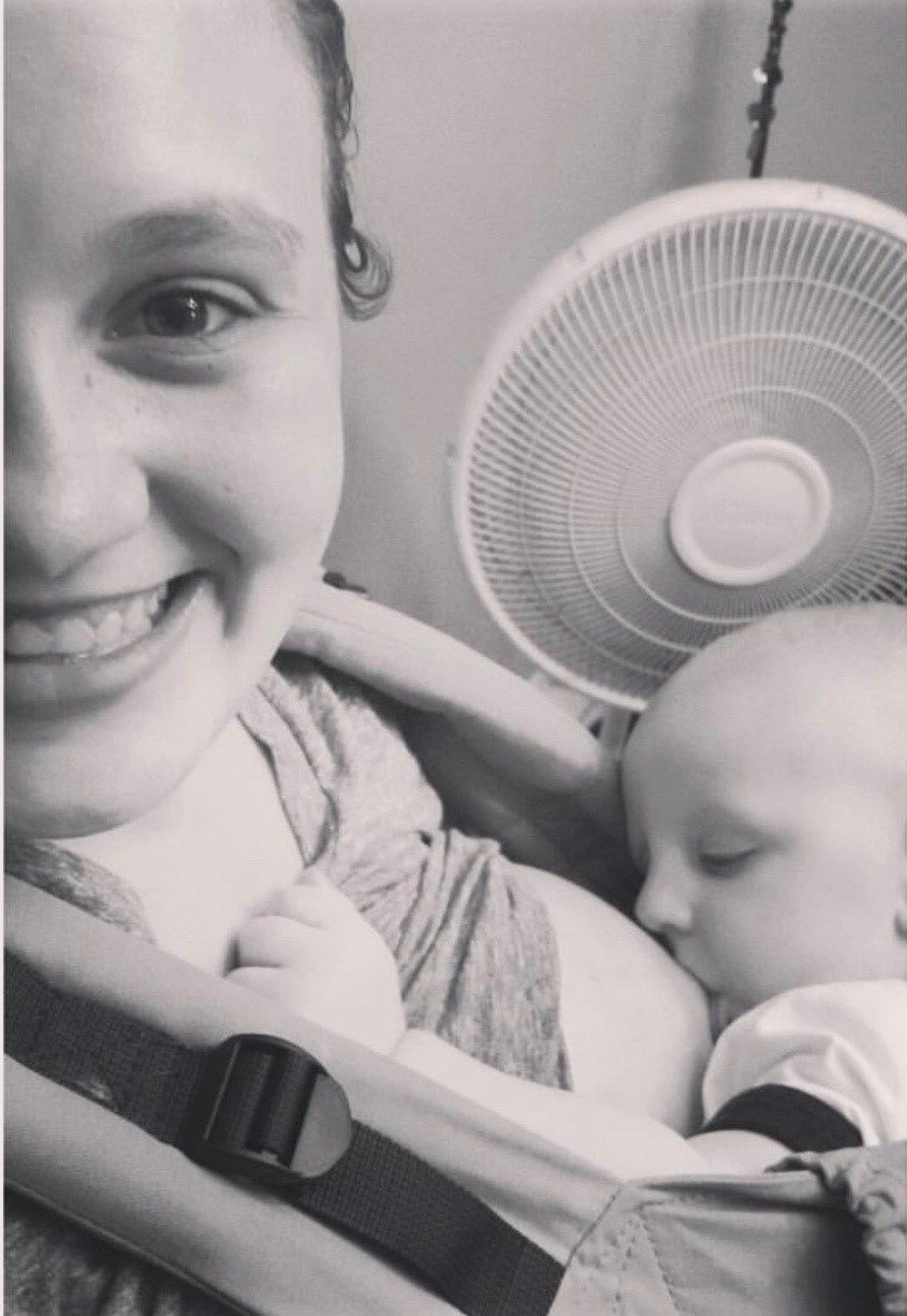 A black and white photo of a smiling mother nursing her baby.