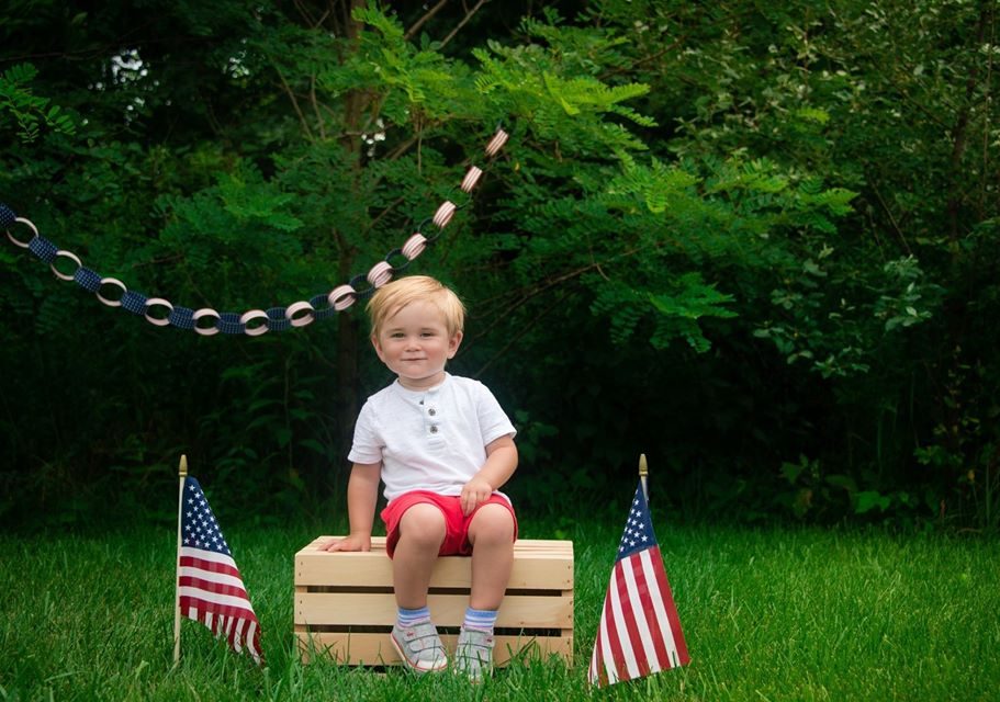 A toddler in a white shirt and red shorts sitting outdoors.