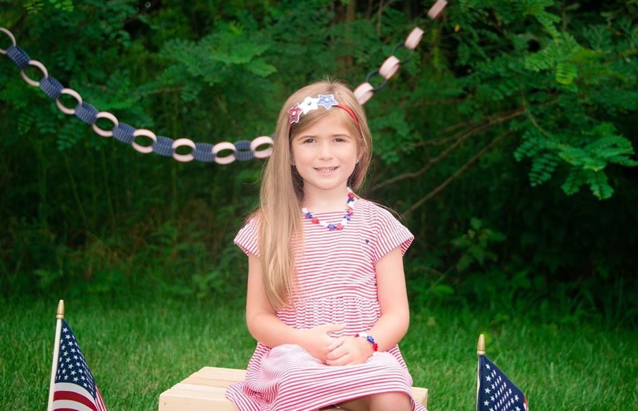 A young girl in a pink dress sitting on a bench outdoors.