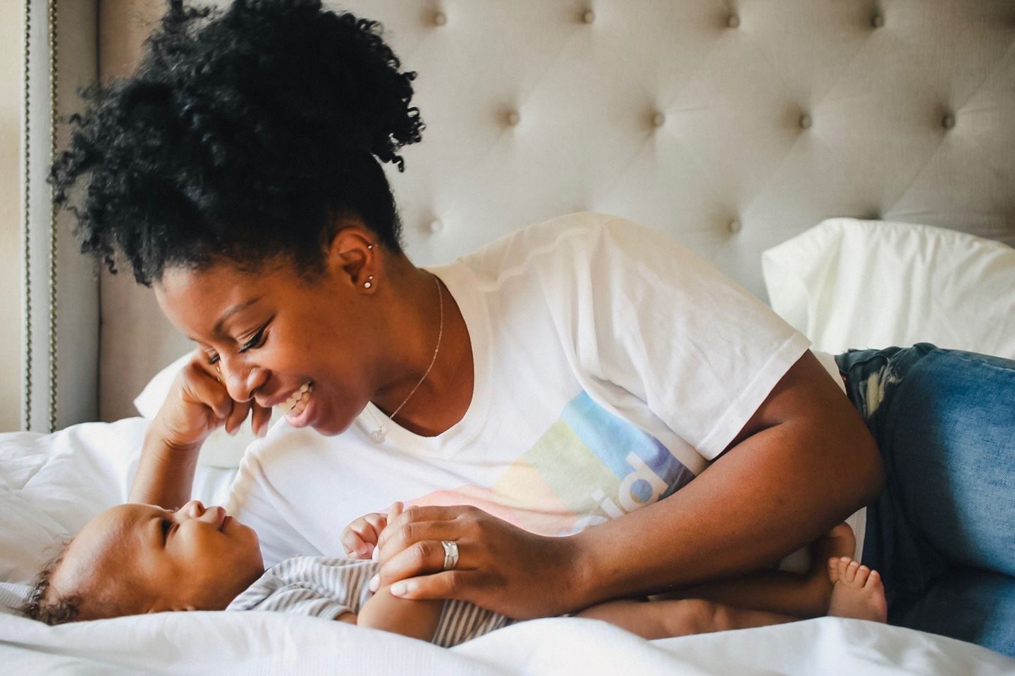 A mother lying on a bed gazing at her newborn beside her.