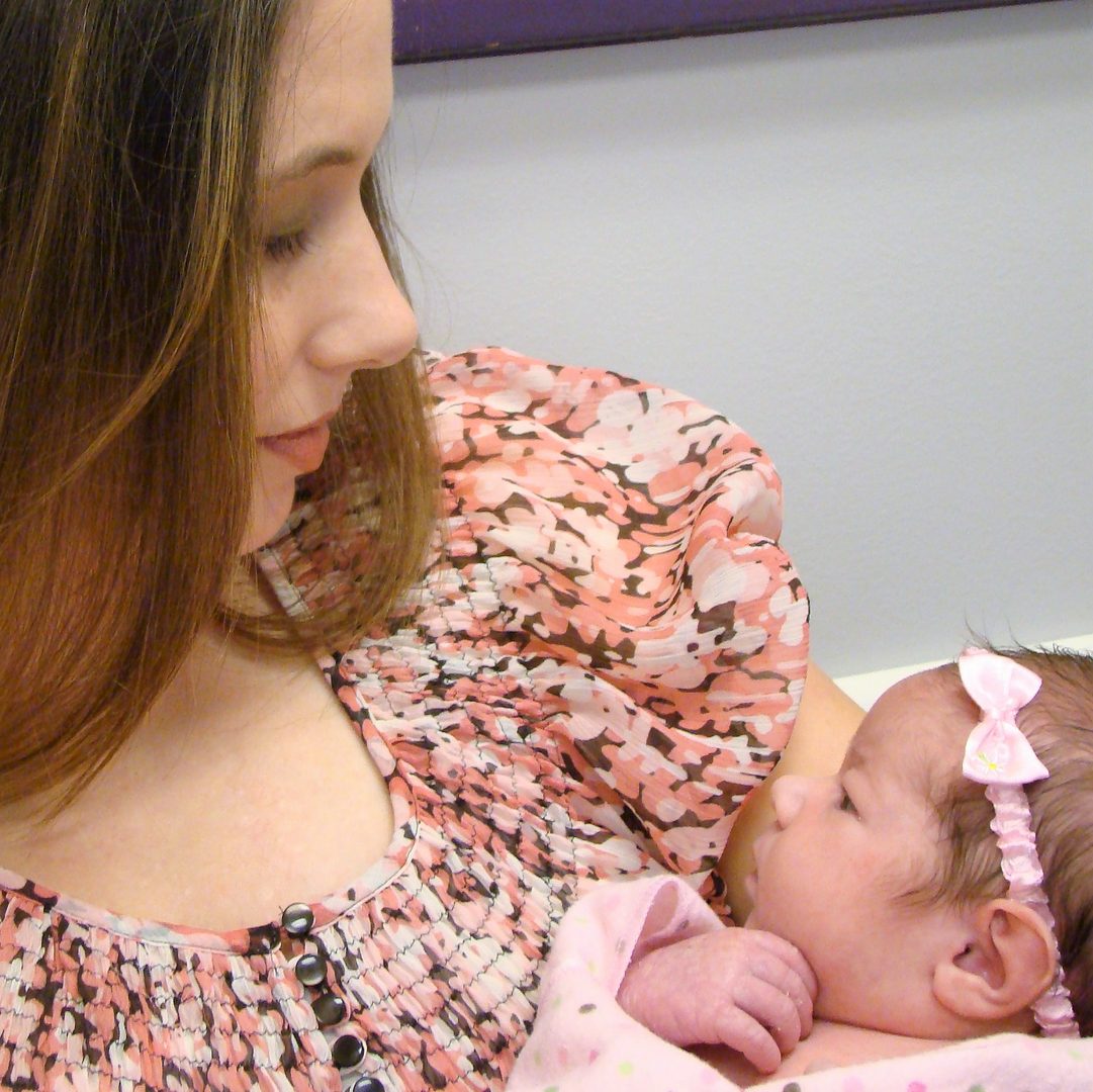 A baby in a floral outfit resting in a parent's arms.