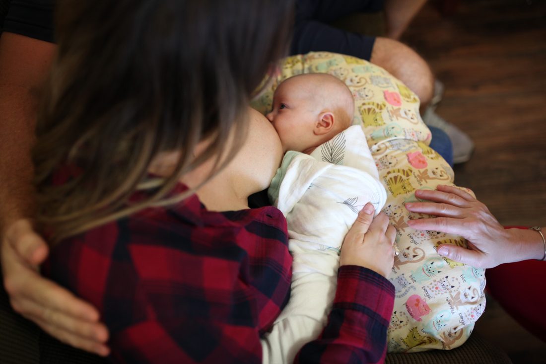 A mother breastfeeding her baby on a nursing pillow.