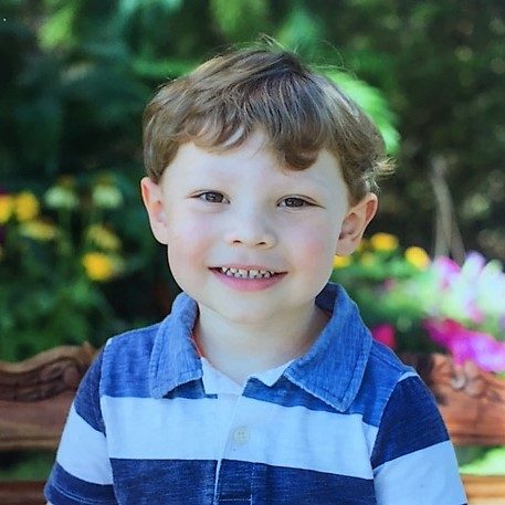 A toddler boy smiling in a blue shirt.