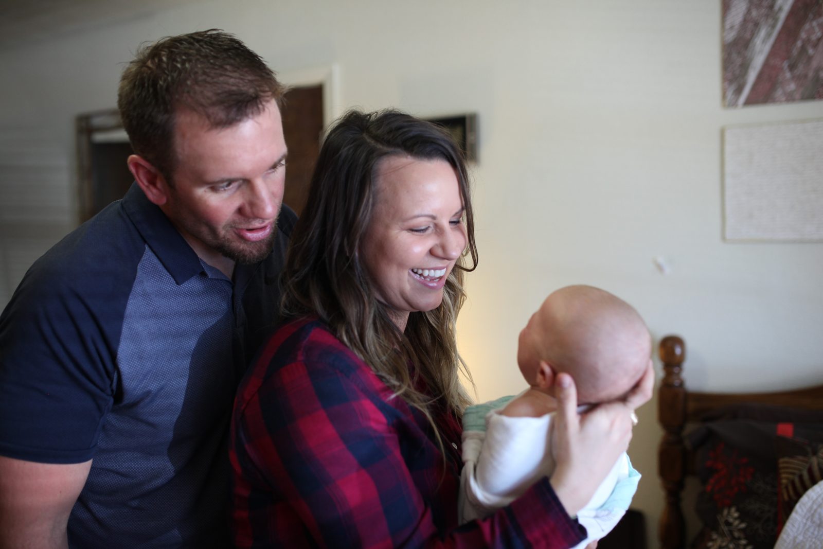 Two parents smiling at their newborn at home.