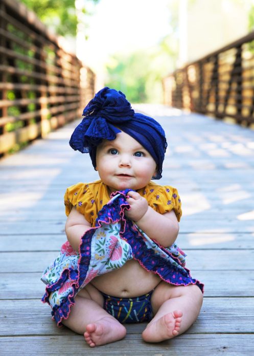 A baby in a bonnet and bow dressed up outdoors.