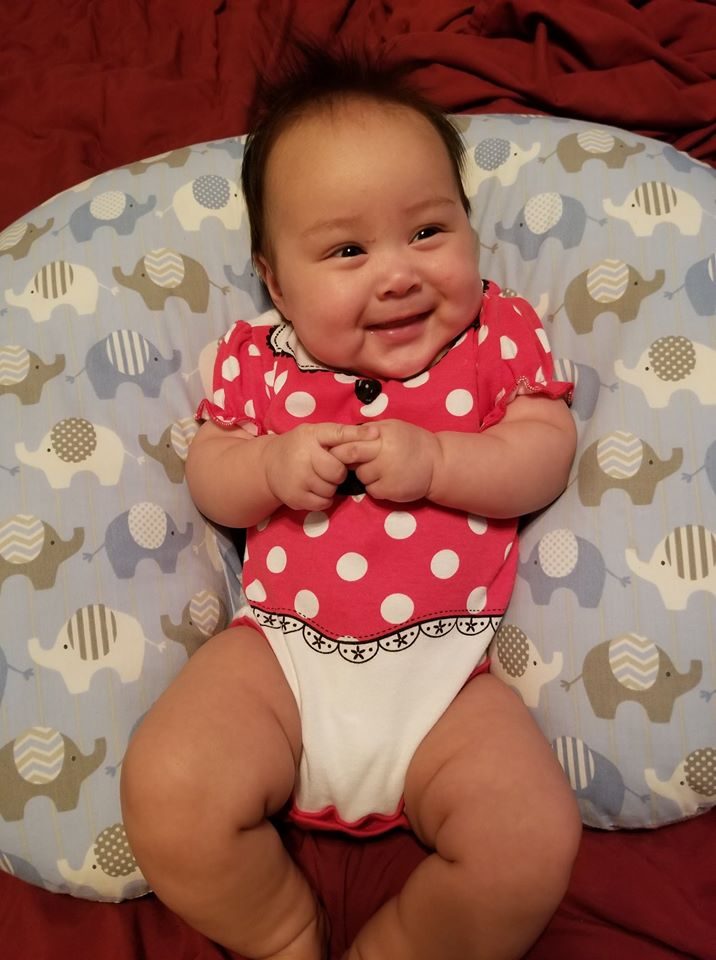 A baby in a red polka-dot outfit reclining in a chair.