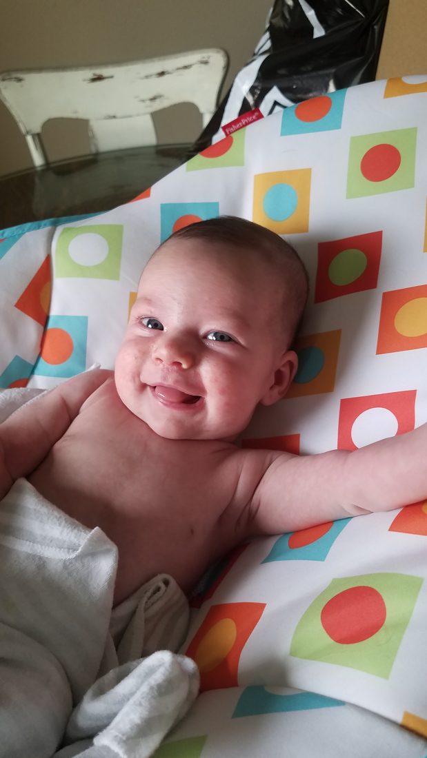 A chubby-cheeked baby smiling against a patterned background.