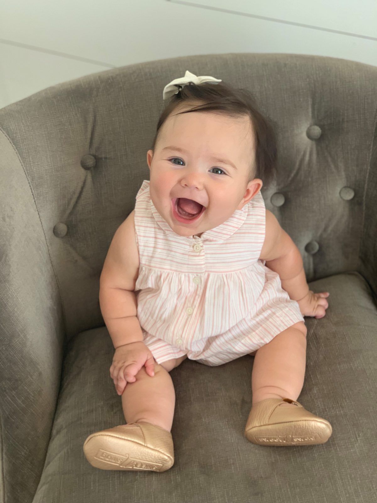 A laughing baby in a striped romper sitting on an armchair.