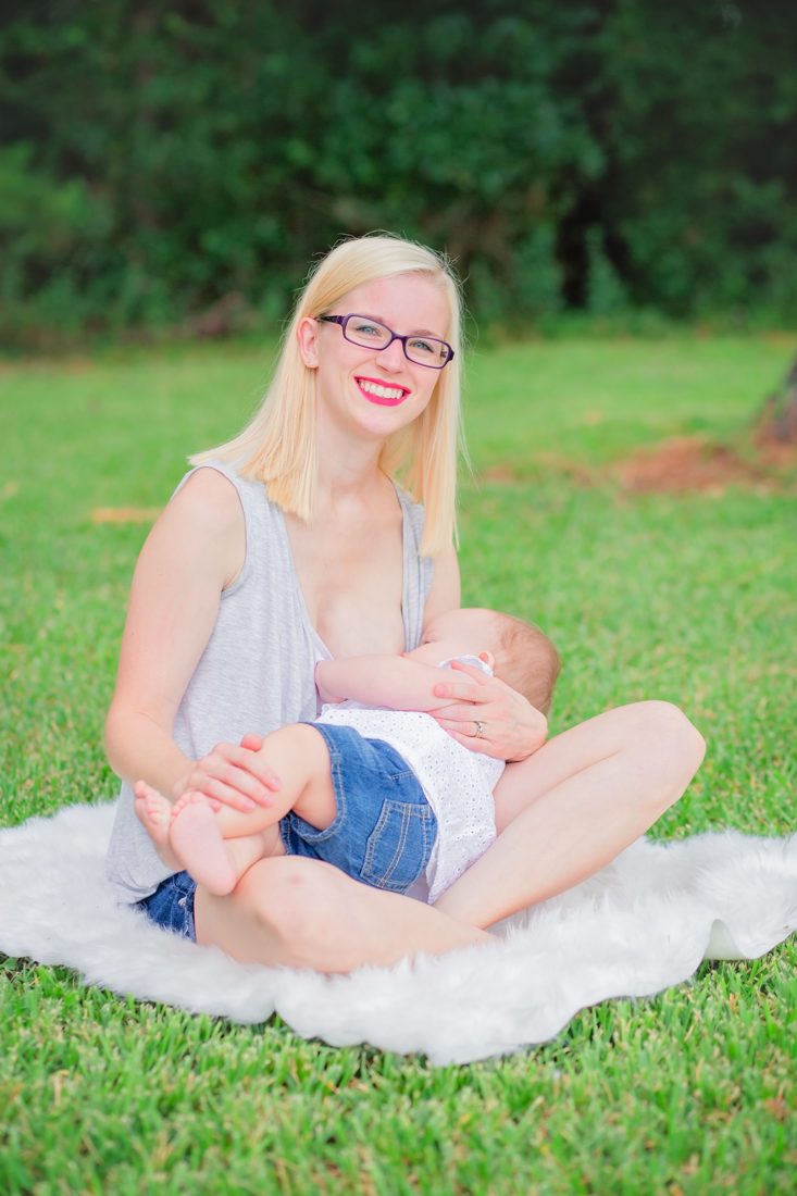 A mother sitting on a blanket holding her baby outdoors.