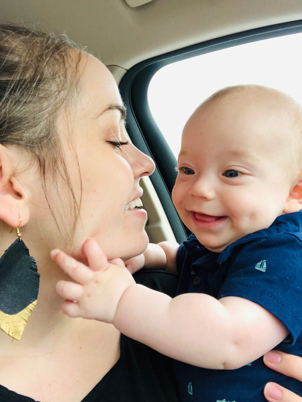 A mother smiling at her laughing baby in a car.