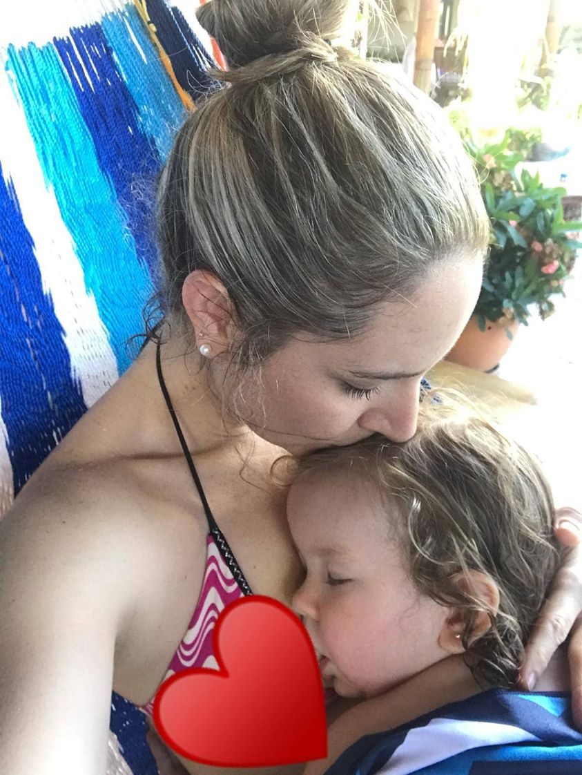 A mother nursing her toddler outdoors against a blue wall.