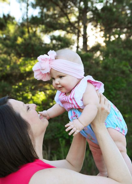 A parent holding a baby in a flower-trimmed outfit outdoors.