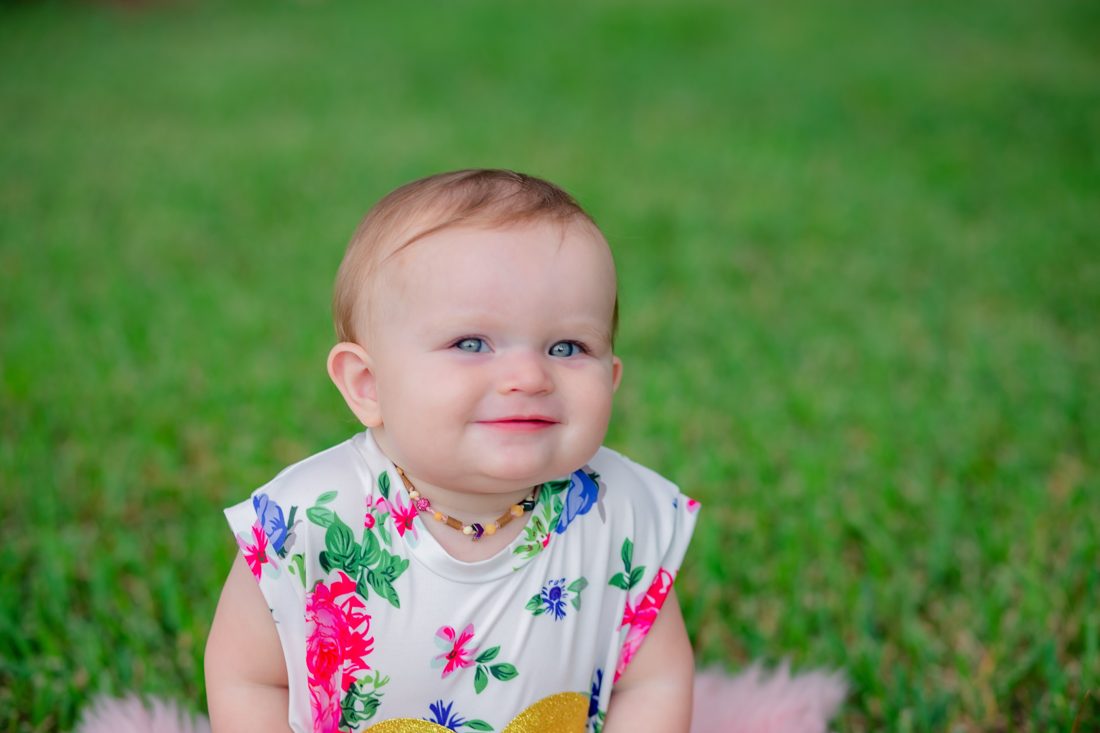 A toddler standing and smiling in a sunny yard.