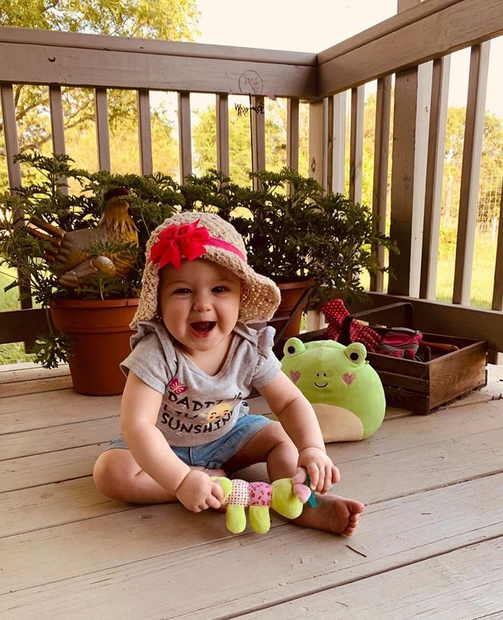 A toddler in a watermelon outfit sitting on the floor playing.
