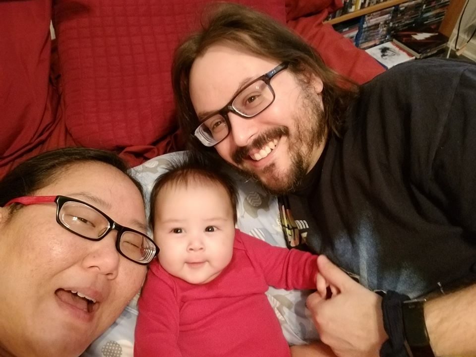 Two parents smiling closely with their baby between them.