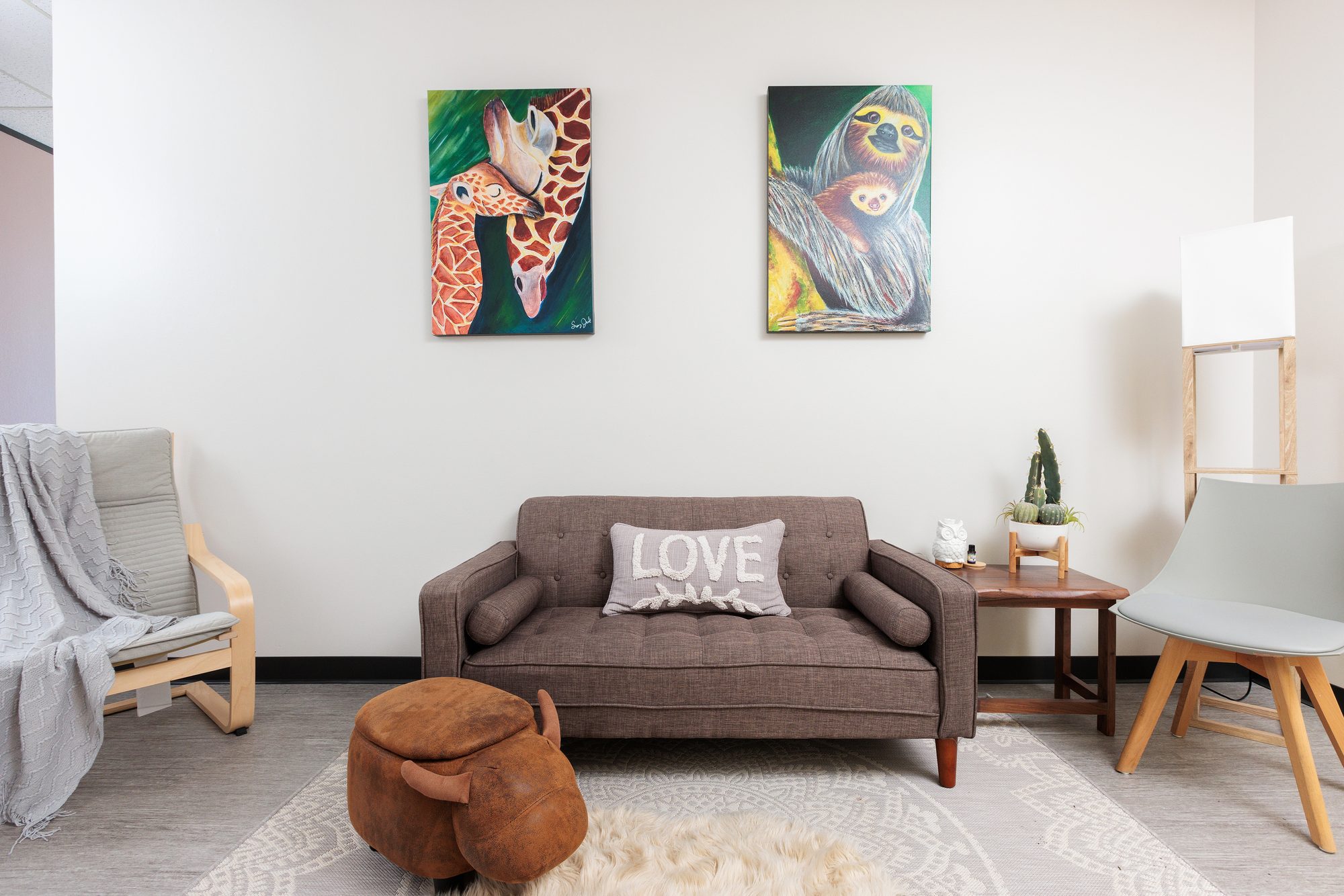 Animal paintings above a grey sofa with a cactus and a grey accent chair