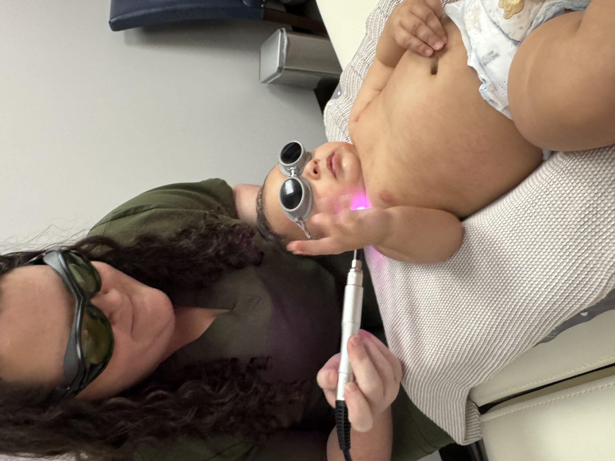 An infant wearing protective laser goggles during a photobiomodulation session with a chiropractic team member